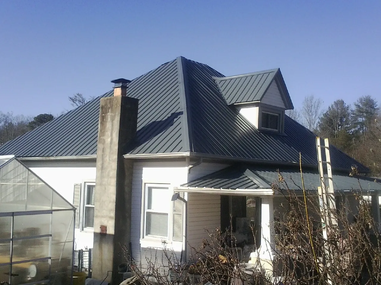 Dark blue standing seam metal roof on a white farmhouse with dormer — Slate & Tile Roof Repair by Roofing Brothers in Cedar Hill