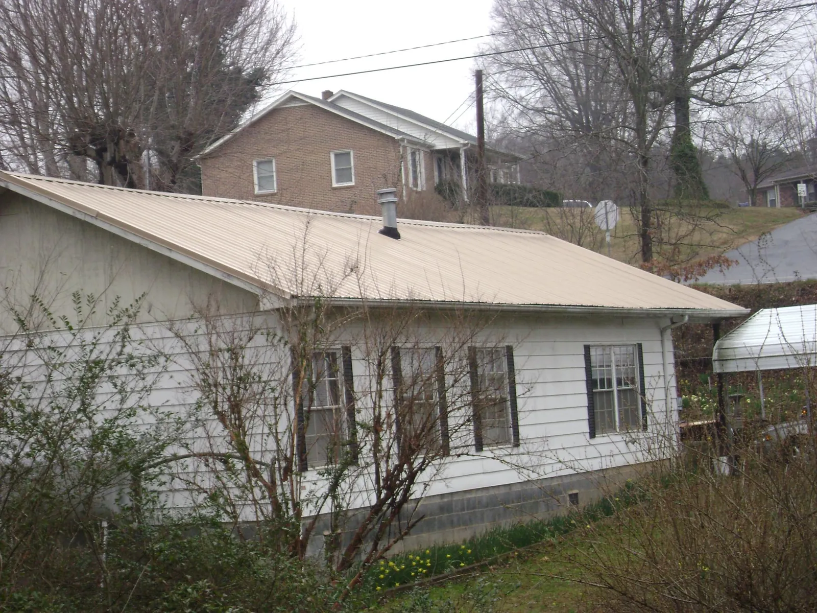 Tan metal roof on a white sided house set into a hillside — Commercial Roofing by Roofing Brothers in Cedar Hill